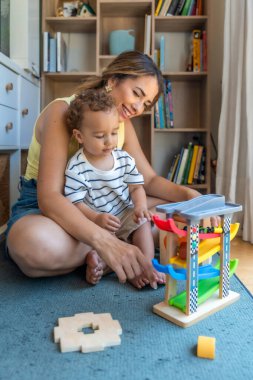 Gülümseyen anne ve oğul oyuncak araba ve garajla oynuyorlar. Oturma odalarında kaliteli vakit geçiriyorlar.