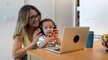 Genç anne ve oğlu kulaklık takıyor ve bir dizüstü bilgisayardan video görüşmesi yapıyorlar. Bu arada çocuk da bir parça meyve yiyor.