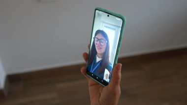 Gözlüklü genç bir kadınla video görüşmesine katılırken elinde modern bir akıllı telefon tutan tanınmayan kişi uzaktan iletişim ve internet üzerinden iş görüşmesi kavramları gösteriyor.