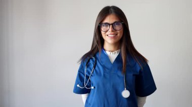 Kameraya bakarken gülümseyen ve kollarını kavuşturan steteskop ve gözlüklü güzel bir bayan doktor ya da hemşire, beyaz bir arka planda izole edilmiş profesyonel bir sağlık çalışanı.