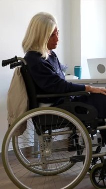 Genç bir kadın doktor, modern bir klinikteki fizik tedavi seansında, tekerlekli sandalyede yaşlı bir kadına yardım ediyor, kapsamlı bir bacak ve ayak muayenesi sağlıyor.