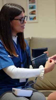 Kadın hemşire, ev ziyareti sırasında profesyonel bakım, sağlık kontrolü ve destek sağlamak için dijital sphygmomanometre kullanarak yaşlı bir kadının kan basıncını ölçüyor.