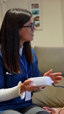 Yaşlı bir kadına evde bakıcılık yapan şefkatli bir hemşire oturma odasındaki kanepede otururken tansiyonunu elektronik tonometreyle ölçüyor.