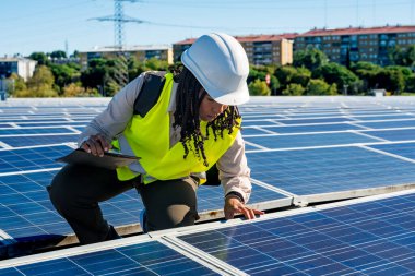 Ticari bir binanın çatısındaki fotovoltaik güneş panellerini denetleyerek yenilenebilir enerji sistemi verimliliğini ve sürdürülebilir işlevini güvence altına alan bir kadın mühendis.