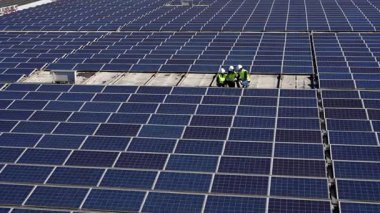 Üç yenilenebilir enerji mühendisi, temiz ve sürdürülebilir elektrik üreten geniş bir fotovoltaik panellerle çevrili bir çatı güneş çiftliğinde iş birliği yapıyorlar.