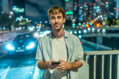 Geceleri dışarıda duran genç adam akıllı telefonuna gülümsüyor, şehir merkezindeki Bokeh 'e gülümsüyor ve arkasında parıldayan araba ışıkları, rahat bir modern yaşam tarzı ve dijital bağlantı ortamı.