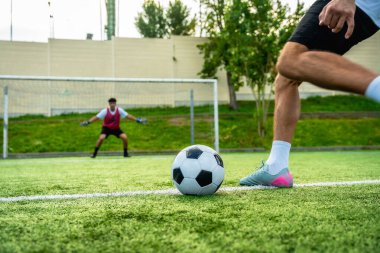 Futbolcu suni sahada topla penaltı atışına hazırlanıyor. Kaleye odaklanmış bir kaleci, yoğun bir atletizm müsabakası yaratıyor.