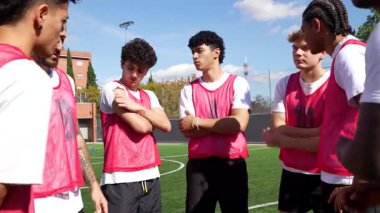 Genç çok kültürlü futbolcular yeşil sahada toplanıp antrenörlerini dinliyor ve maçtan önce taktikleri tartışıyorlar. Amatör sporlar için takım çalışması ve iletişim konsepti