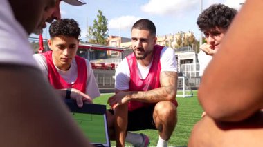 Profesyonel koç antrenman sırasında futbol takımıyla taktikleri tartışır. Oyun planını açıklamak ve yeteneklerini geliştirmek için saha diyagramını içeren bir pano kullanır.