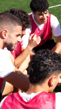 Futbol koçu, genç erkek oyunculardan oluşan çeşitli takımına dijital tabletle oyun taktiklerini açıklarken şampiyonluk maçından önce güneşli bir günde yeşil sahada toplandı.