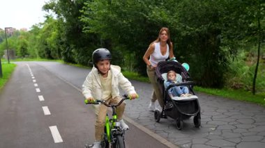 Mutlu bir aile birlikte dışarıda eğleniyor. Çocukken annesiyle birlikte bisiklet sürmeyi öğreniyor. Yanında yürüyor, bebekle bebek arabasını itiyor.
