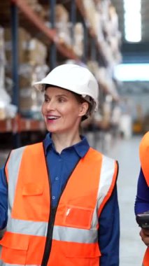 İki farklı kadın depo çalışanı stokları kontrol etmek ve büyük bir lojistik merkezinde yürürken el bilgisayarlı barkod tarayıcısı kullanarak envanter yönetimi üzerinde çalışıyor.