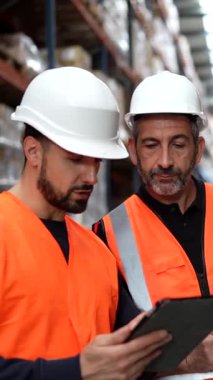 Envanteri yönetmek ve raflar arasındaki depolama prosedürlerini açıklamak için dijital tablet kullanan büyük bir dağıtım merkezinde yeni bir işçiye danışmanlık yapan profesyonel lojistik danışmanı