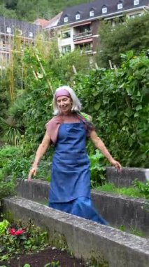 Enerjik, üst düzey bir kadın neşe içinde dans ediyor ve yemyeşil bir halk bahçesinde yürüyor, hasatını kutluyor ve şehir binaları arasında sürdürülebilir bir yaşam tarzının tadını çıkarıyor.