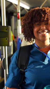 Güneşli bir günde halka açık bir otobüste giderken gülümseyen kıvırcık saçlı güzel siyah hemşire. İş seyahatinde ya da seyahatinde olan sağlık uzmanı, günlük yolculuğunun keyfini çıkarıyor.