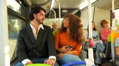 Güzel, çok kültürlü bir çift modern bir halk otobüsünde birlikte seyahat ederken konuşuyor ve gülümsüyor, yolculuklarının keyfini çıkarıyor ve güneşli bir günde pencereden içeri güneş ışığı giriyor.