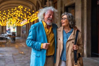 Kıdemli çift kemerli bir şehir geçidinde kol kola yürüyorlar, neşeli ışıklar altında gülümsüyor ve gülüyorlar, sıcak, samimi bir aşk ve arkadaşlık anlarını paylaşıyorlar.