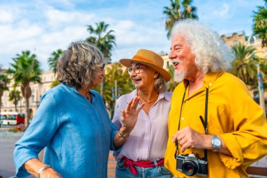 Üç neşeli kıdemli arkadaş şehir tatili boyunca dışarıda canlı bir tartışmanın tadını çıkarıyorlar. Palmiye ağaçları altında kahkahalar ve güzel zamanlar geçiriyorlar ve parlak bir gökyüzü.