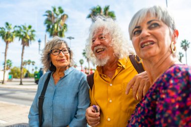 Üç kıdemli arkadaş, şehir sokaklarında yürürken tatilin tadını çıkarıyorlar. Anları paylaşıyorlar ve tartışıyorlar. Arka planda palmiye ağaçları açık bir gökyüzünün altında görülebiliyor.