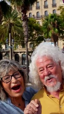 Neşeli bir grup yaşlı arkadaş, güneşli bir günde aktif ve neşeli bir emeklilik yaşam tarzını kucaklayarak güzel bir şehirde selfie çekerken gülüp eğleniyorlar.