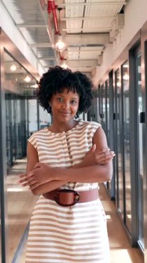Profesyonel Afro saçlı Amerikalı kadın modern bir ofis koridorunda durup gururla kameraya bakarken kollarını kavuşturarak güvenle gülümsüyor.