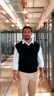 Genç Afrikalı Amerikalı girişimci modern cam ofis koridorunda duruyor, güvenle kollarını kavuşturup kameraya gülümsüyor, pozitif ve başarılı bir iş tutumu sergiliyor.