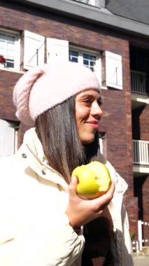 Güneşli bir şehir sokağında dikilen sıcak bere ve ceketler giyen iki neşeli arkadaş, güz mevsiminde birlikte taze kırmızı ve yeşil elmalardan oluşan sağlıklı bir aperatifin tadını çıkarıyor ve sohbet ediyorlar.