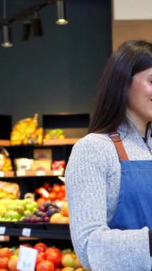 Mavi önlüklü ve siyah eldivenli genç bir esnaf yerel bir marketten ya da çiftçi pazarından taze, olgun sebzeleri seçen bir kadına yardım ediyor.