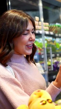 Marketteki vitrinden taze, olgun şeftalileri seçen genç bir kadın satın almasına yardım eden dost canlısı bir kadın manavın yardımıyla.