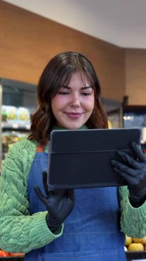 Bir marketin taze üretim bölümünde dijital tablet kullanan önlüklü, arkadaş canlısı bir manavdı. Mükemmel bir hizmet sunuyordu.