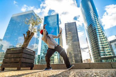 Afrika kökenli Amerikalı adam, Los Angeles şehir meydanında modern dans gösterisi yapıyor. Camdan gökdelenlere karşı tam boy siluet ve parlak mavi bir gökyüzü. Hareket, neşe ve modern enerji taşıyor.