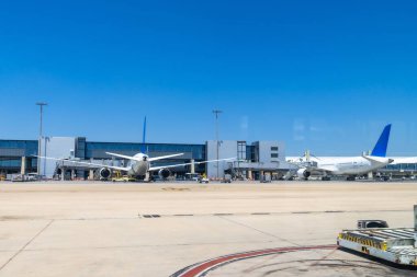 İki büyük yolcu uçağı havaalanı kapılarına parlayan güneşli gökyüzünün altında yolcuları bekliyor ve hareketli bir yolculuk günü için hazırlanıyorlar.