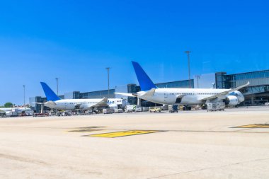 Güneşli bir günde modern bir havaalanının kapısına park edilmiş iki büyük yolcu uçağı, bir sonraki uçuşları için bakım ve hazırlık aşamasında.