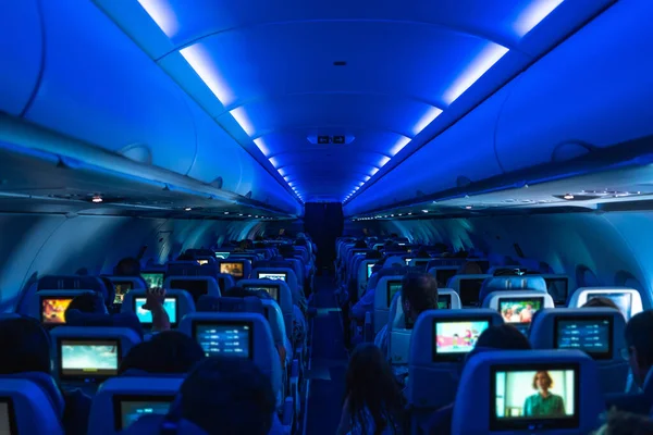 Uçak kabinindeki mavi çevre aydınlatması altında rahat bir atmosferle çevrili kişisel ekranlardan film izlerken uçuş eğlencesinin tadını çıkaran yolcular