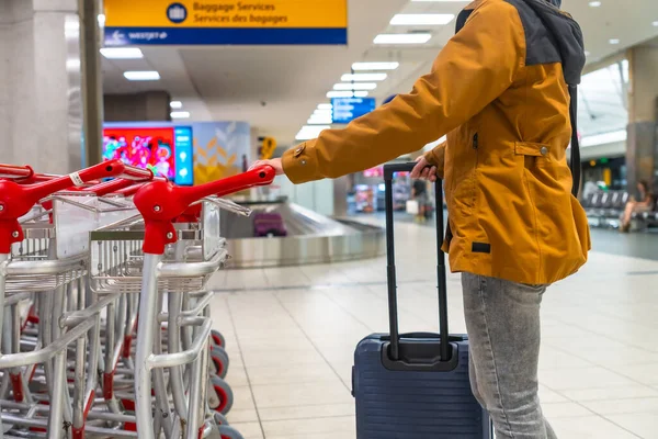 Tourist is pulling his trolley suitcase and taking a luggage cart at the airport terminal, near the baggage claim area, getting ready for his trip
