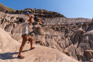 Turist baba, güneşli bir günde, Kanada 'nın çorak bölgelerinde, davulcu kabadayılarının eşsiz jeolojik oluşumları önünde oğlunu havaya kaldırarak eğleniyor.