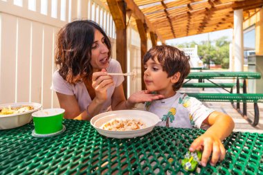 Mother feeds her son at a picnic table outside a restaurant in drumheller, alberta, canada, creating a heartwarming moment of family connection