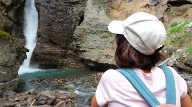 Kükreyen Johnson Canyon Şelalesi 'nin yanında duran kadın turist yaz aylarında Kanada kayalıklarında yapılan keşifler sırasında Banff Ulusal Parkı' nın el değmemiş vahşi doğası ile çevrilidir.