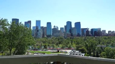 Calgary 'nin etkileyici silueti görkemli bir şekilde yemyeşil şehir parkının üzerine yükseliyor, berrak mavi gökyüzüne karşı canlı bir şehir manzarası sergiliyor, hafif değişen bir bakış açısı sunuyor.
