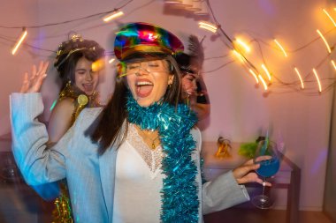 Canlı bir yeni yıl arifesinde ya da kostüm partisinde, neşeli atmosferin ve renkli ışıkların tadını çıkararak birlikte dans eden ve gülen üç neşeli genç kadın.