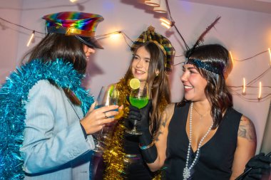 Üç mutlu genç kadın yeni yıl arifesinde eğleniyor ya da içkiler ve süslü süslemelerle kostüm partisi veriyor, gülümsemeleri paylaşıyor ve birlikte neşeli kutlama anları yaratıyorlar.