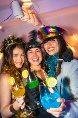 Üç mutlu genç kadın yeni yıl arifesini kutluyorlar, neşeli kostümler giyiyorlar ve canlı bir parti atmosferinde limonlu süslemelerle renkli içecekler içiyorlar.