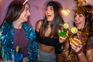 Parti dekorasyonlarıyla kutlama yaparken gülen ve kokteyl içen bir grup kadın, ya da arkadaşlarla eğlenen bir kostüm partisi, neşe ve dostluk dolu.