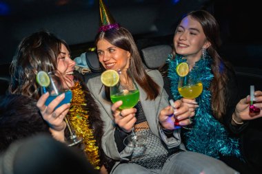 Genç kadınlar yeni yıl arifesini bir partiye giderken ellerinde renkli kokteyller, şen şakrak giyinmiş, gece yolculuklarının tadını çıkarıyorlar.