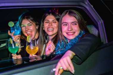 Genç bayan arkadaşlar gülümsüyor ve eğleniyorlar canlı bir yeni yıl partisinde ya da kutlamalarında, gece araba sürerken renkli kokteyller içiyorlar, beraberliğin ve gece hayatının tadını çıkarıyorlar.