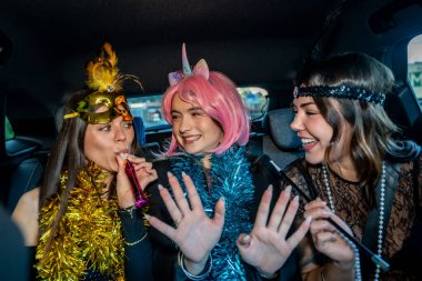 Şenlikli kostümlü üç genç kadın bir arabaya biniyor. Süslü ve makyajlı. Birlikte neşeli bir geceyi kutlarken gülüyor ve parti üflüyorlar.