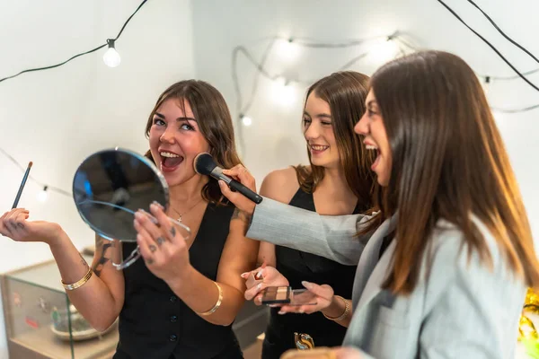Üç mutlu genç kadın makyaj yapıyor ve birlikte gülüyor, gülümsüyor ve evde özel bir etkinliğe ya da şenlik toplantısına hazırlanıyor.