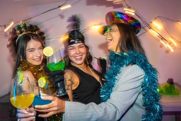 Üç gülümseyen genç arkadaş parti kostümleri ve şenlikli aksesuarlar giyip neşeli içkilerle özel bir olayı kutluyorlar. Neşeli bir gecenin tadını çıkarıyorlar.