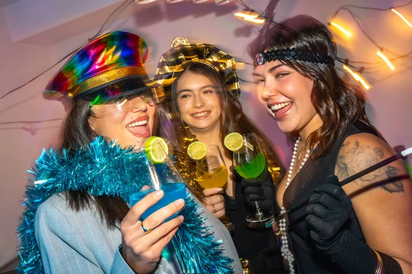 Üç mutlu genç kadın yeni yıl arifesini kutlarken ve renkli kokteyller içerken ya da şenlikli süslemeler ve parlak ip ışıklarıyla kostüm partisinde.