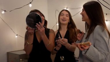 Birlikte makyaj yaparken gülen ve gülümseyen üç güzel genç kadın, bir partiye ya da festival ışıklarıyla süslenmiş bir odada kızlar gecesine hazırlanıyorlar.